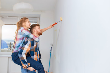 Young couple, having no many for professional painter and ladder, making fun, as a young woman piggybacking on her husband to gain extra height when painting the wall at their home
