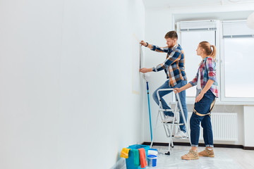 Full-size view of a woman looking while man measuring the wall at new home. House Renovation DIY...
