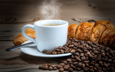 a Cup of coffee on a wooden table with scattered coffee beans and a croissant