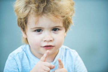 Child with fingers shows up. Beautiful baby face. Child portrait. Blond preschooler. Smart child looking into the camera.