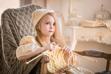 little girl, child, blonde with long hair, in light vintage clothes, knitting on knitting needles from thick yarn