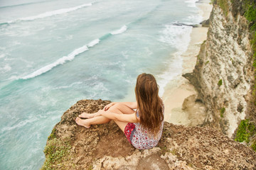 A young girl is sitting on a cliff. Bali, Uluwatu. 