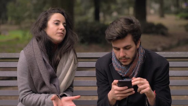 Annoying girlfriend talking while boyfriend ignoring her using smartphone-outdoo