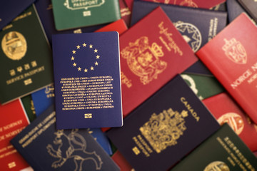 Blue biometric passport of the European Union on a blurred background of mixed passports from around the world - obrazy, fototapety, plakaty