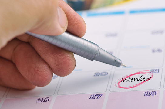 Time planning concept,  cropped hand and yellow sticky paper with word INTERVIEW on calendar