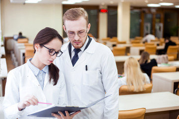 Obraz premium Joyful young general practitioner. Smiling professional doctor in white coat discussing diagnosis in library. Health concept