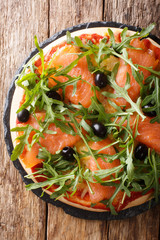 Delicious pizza with salted salmon, arugula, olives and cheese closeup. Vertical top view