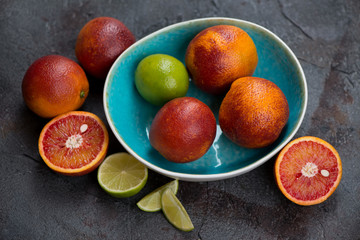 Turquoise bowl with blood oranges and limes on a grey asphalt background, studio shot