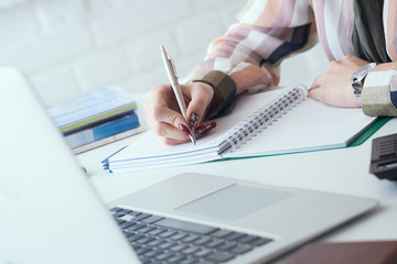 Side view of business woman making notes with silver pen in office background. Business finance savings loan and credit concept.