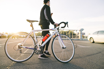 Portrait of a rider on the back with a white highway bike, background of the street at sunset. Cyclist in black sportswear goes with a bike.