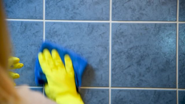 Women's hands in yellow gloves clean tiles