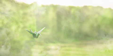 paper origami cranes. garland of origami birds hanging on natural background. spring or summer season. beautiful inspiring nature image. asian culture. gentle toning. banner. soft selective focus. 