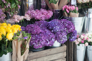 Pots with beautiful blooming pink and purple hydrangea flowers for sale outside flower shop. Garden store entrance decorated with rustic style wooden box and wicker flower pot.