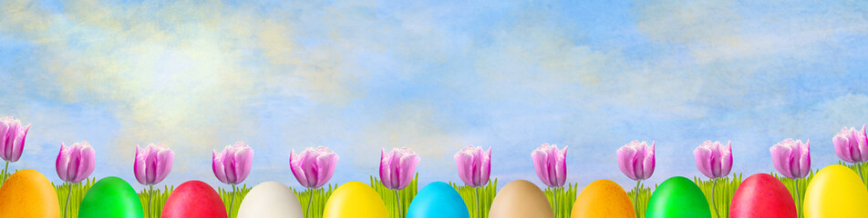Beautiful tulips and colorful Easter eggs on a sunny cloudy sky. Easter background. Happy Easter banner.