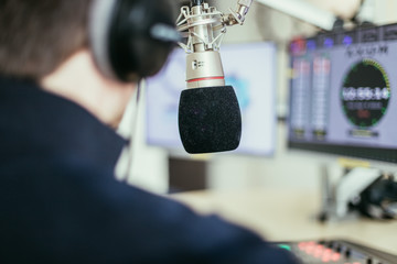 Radio moderator is sitting in a modern broadcasting studio and talking into the microphone