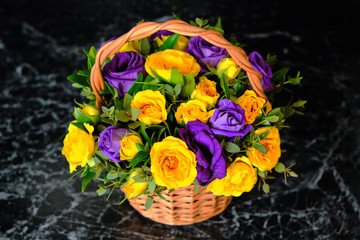 Beautiful bouquet of roses on black marble. Yellow and blue flowers in a wicker basket. Unusual composition of collected violet and yellow flowers.