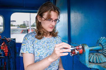 The girl looks at the mechanism in the train in surprise. A woman's hand turns the detail of the steam locomotive. Female portrait on the background of old mechanisms, lifestyle.