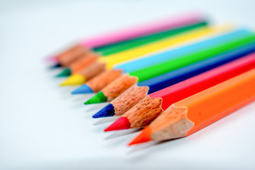 Standing Out From The Crowd Concept. Bunch of assorted multi colored pencils crayons in rainbow arrangement on white background, flat lay. Geometry pattern art design. Selective focus, blur image.