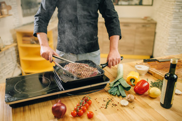 Male person cooking meat in a pan on the kitchen