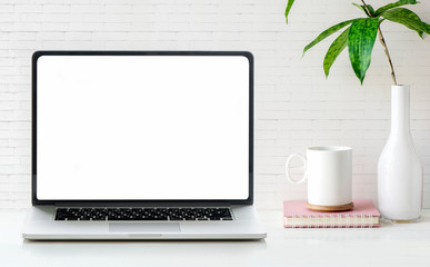 Fototapeta premium Mockup blank screen laptop with cup, book and houseplant on white table and brick wall.