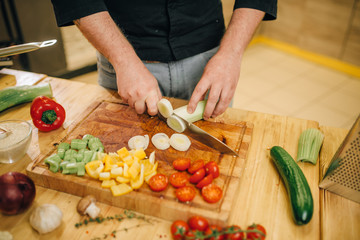 Chef with knife cuts mushrooms on wooden board