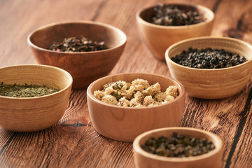 assortment of dry tea in white bowls on wooden surface