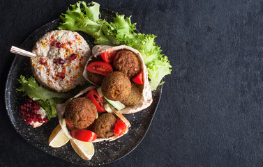 homemade hummus, falafel in pita and tahini with fresh tomato salad and spices on a black chopping Board. Jewish and Arabic cuisine. The concept of vegetarian food. The view from the top. Copy space