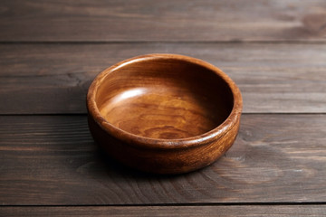 Empty wooden bowl on brown table. Round salad-bowl
