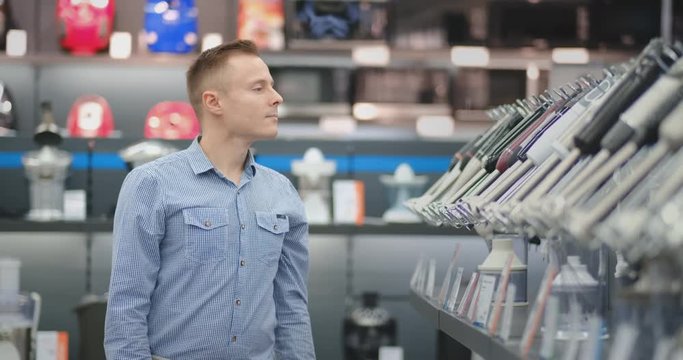 A young man in a shirt chooses a blender for his kitchen in a consumer electronics store