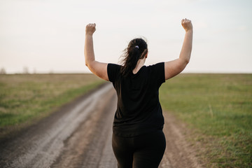 Body positive, freedom, high self esteem, confidence, happiness, inspiration, success, positive affirmation. Overweight woman celebrating rising hands to the sky on summer meadow. - obrazy, fototapety, plakaty