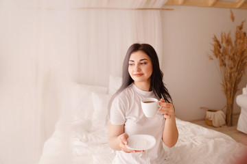Obraz na płótnie Canvas Woman holding a coffee mug at home. Young smiling girl enjoy morning coffee in bed. Daily routine, starting new day, good mood and harmony