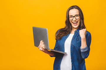 Successful woman with a laptop computer and arms up - isolated over yellow