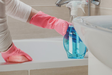 Housemaid in the rubber gloves cleaning bathroom with a sponge