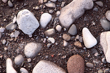 Fototapeta na wymiar Top view on the pebbles of different sizes on the dark volcanic sand. The concept of nature. Cropped shot, close-up, horizontal.