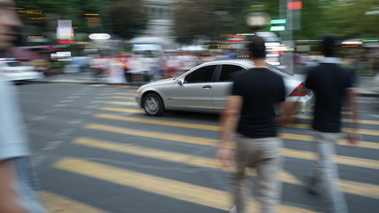 Pedestrians in motion blur crossing a city street while the car is driving at a red light
