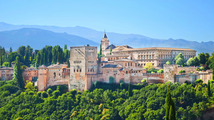 Fototapeta na wymiar Beautiful Alhambra Palace complex in Spanish Granada on a sunny day captured on 16:9 photography. The amazing fortress and popular tourist spot is surrounded by green woods and mountains.
