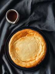 Plate with whole cheesecake pie on table with tablecloth. Classic cheesecake, caramel and dessert forks. Vertical. Top view or flat lay.