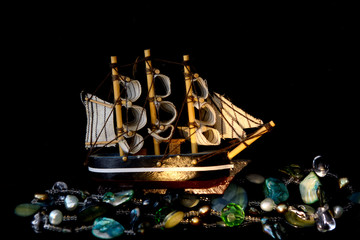 A model of a sailing ship stands on a necklace resembling a sea wave. Concept - hunt for underwater treasure