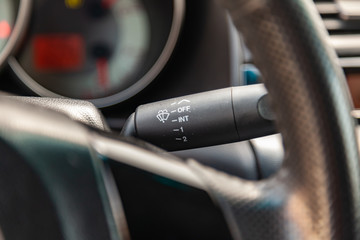 The interior of the car with a view of the steering wheel, dashboard and windscreen wiper switch with light gray trim