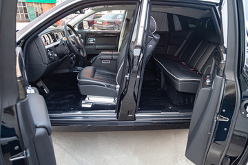 Interior view of new a very expensive car, a long black limousine with opened doors, dashboard, steering wheel, seats on parking