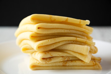 Pile of tasty blini on a white plate, side view. Close-up.