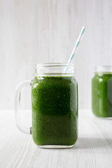 Green smoothie with spinach, avocado and banana in glass jars on a white wooden background, side view. Close-up.