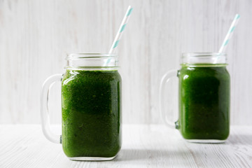 Green smoothie with spinach, avocado and banana in glass jars on a white wooden surface, side view. Close-up.