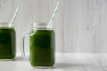 Green smoothie with spinach, avocado and banana in glass jars on a white wooden background, side view. Copy space.