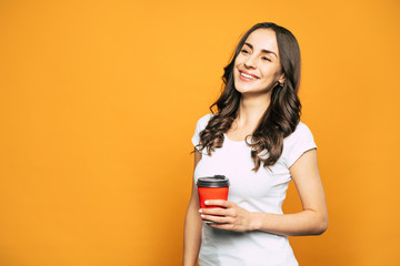 Invigorating coffee. Fabulous girl with the red cup in her hand full of coffee is smiling right next to the spicy-colored background.