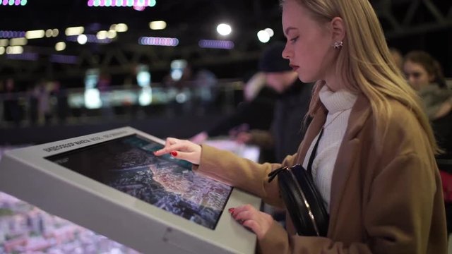 Woman using interactive touchscreen display at urban exhibition - scrolling and touching. Entertainment and technology concept