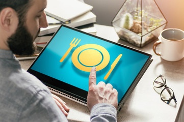 Bearded man with laptop at his desk. He presses on the restaurant icon. Concept of food order via...