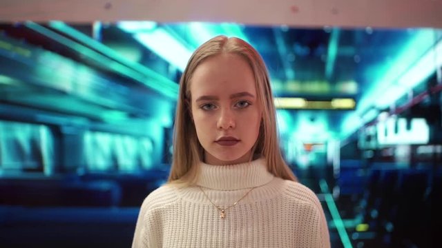 Attractive young woman in white sweater looking to the camera and smiling on the cool neon future theme background. Close up. Portrait shot