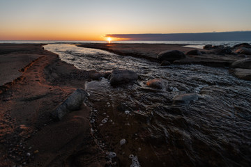Beautiful sunset with red sand and spring water from a river exiting to the sea - Veczemju Klintis, Latvia - April 13, 2019