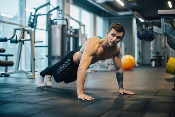 Strongman with naked torso doing push-ups in gym